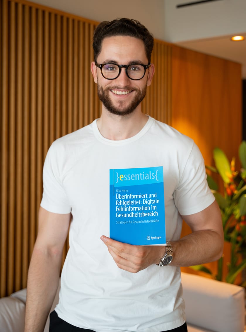Niko Hems holding his book Überinformiert und fehlgeleitet: Digitale Fehlinformation im Gesundheitsbereich (Springer essentials)